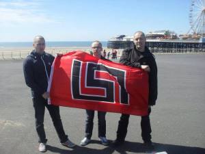 Dumont (centre) posing with the flag of Greek fascist party Golden Dawn